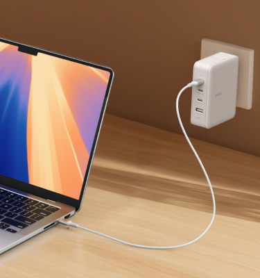 A MacBook charges on a wooden desk using the Belkin GaN Wall Charger and USB-C Cable bundle, delivering high-speed power through a sleek, space-saving design.