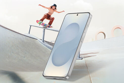 Smartphone standing upright in the foreground at a skate park, with a skateboarder performing a trick on a ramp in the background.