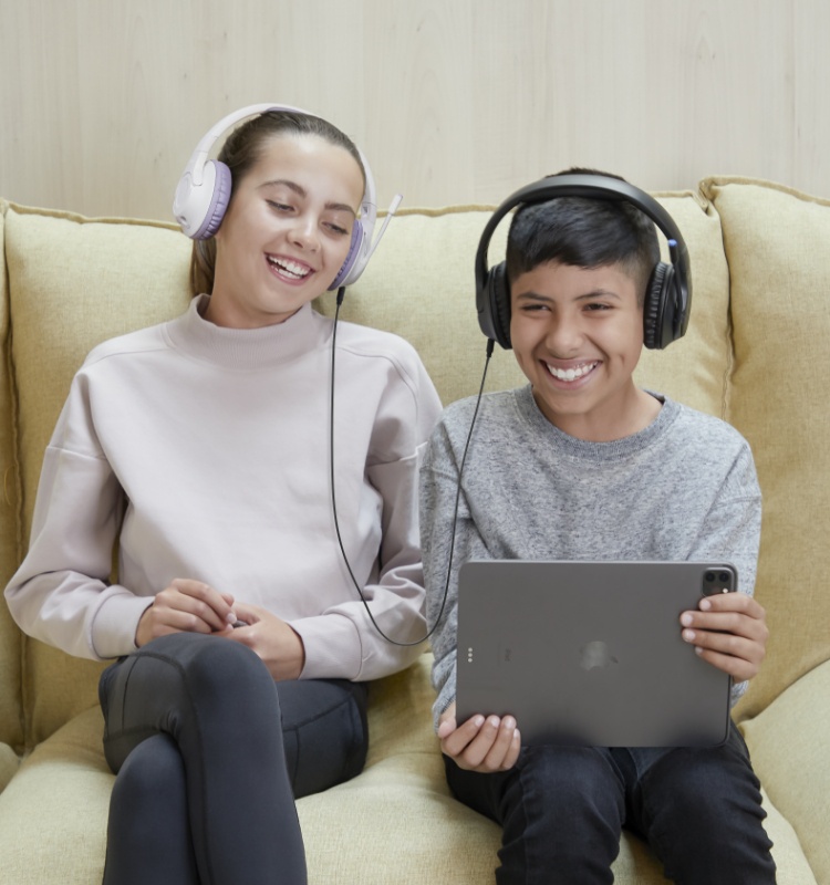 An image of two children, both wearing Belkin Wireless Over-Ear Headsets for Kids, listening to audio from the same device.