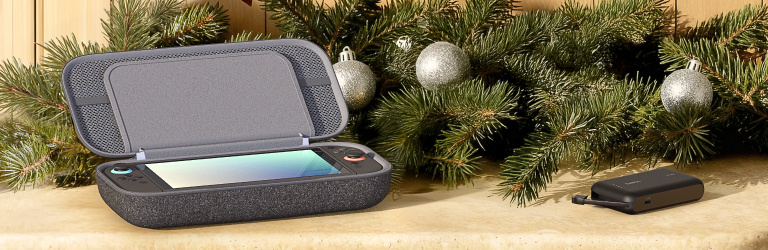 Holiday banner featuring gaming tech gifts, including a handheld gaming console in a gray protective case and a compact Belkin accessory, set against festive greenery with ornaments.