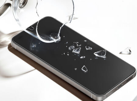 Smartphone lying on a white surface with shards from a broken glass resting on the screen, illustrating scratch and impact resistance.