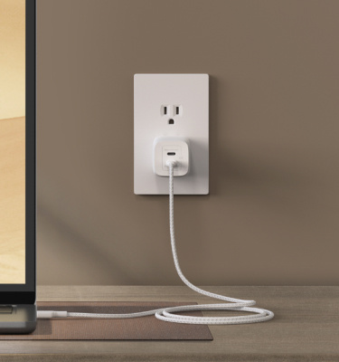 Belkin Fast-Charging USB-C Cable and GaN Charger Bundle plugged into a wall outlet powers a laptop efficiently on a modern desk setup.