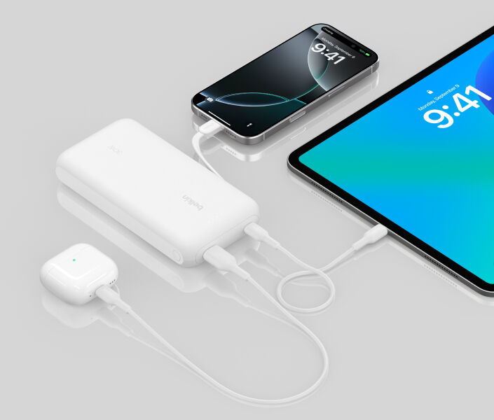 反射面上に配置されたホワイトのBelkin BoostChargeモバイルバッテリー20K（一体型ケーブル付き）で、iPhone、iPad、AirPodsを同時に充電する様子が示されています。