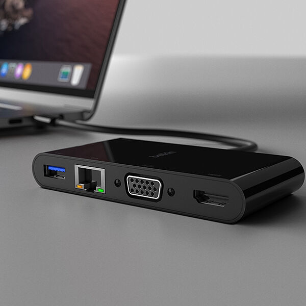 A black multi-port docking station connected to a laptop, featuring various ports including USB-A, Ethernet, VGA, HDMI, and an audio jack. The docking station is placed on a sleek grey desk, providing expanded connectivity options for the laptop in the background.