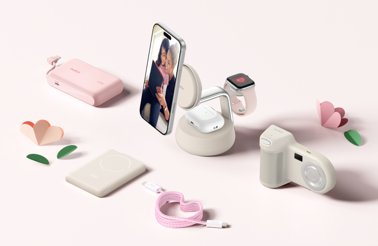 Belkin Mother&rsquo;s Day desktop banner featuring wireless charging stand with iPhone, Apple Watch, and AirPods alongside portable power bank, magnetic charger, cable, and compact camera in soft pink lifestyle setting.