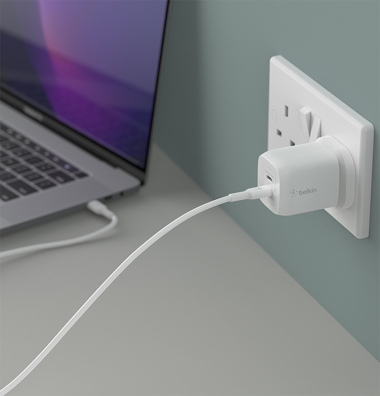 An image of a Belkin Dual USB-C® GaN Wall Charger with PPS 65W in use, plugged into a wall outlet with USB-C cable plugged into bottom port. 