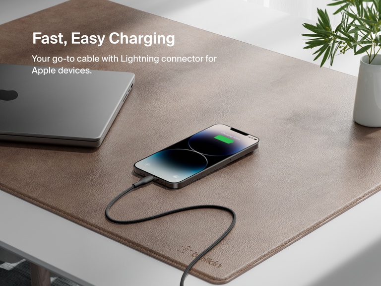 A Belkin BoostCharge Braided USB-A Cable with Lightning Connector charges an iPhone on a desk, showcasing fast, reliable charging for Apple devices.
