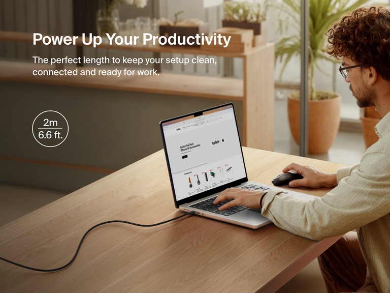 Man working at a desk with a laptop powered by the Belkin BoostCharge Pro USB-C to USB-C Braided Cable 240W, shown in a 2-meter (6.6 ft) length for an extended and clutter-free workspace.