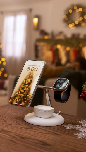 The image features an iPhone, Apple Watch, and wireless earbuds charging on a Belkin BoostCharge Pro 3-in-1 Magnetic Wireless Charging Stand with Qi2 15W, set against a festive background of a decorated living room with a Christmas tree, wreaths, and stockings.