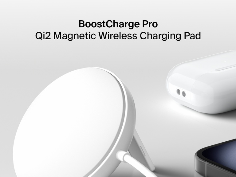 白い台の上で、Belkin BoostChargeマグネット式ワイヤレス充電パッド（Qi2 15W、ホワイト）が、iPhoneと充電ケースに入ったペアの白いAirPodsの横に直立しています。
