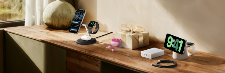 Belkin wireless charging stands, wall charger, and braided cable displayed on a wooden surface beside a wrapped gift in a cozy lifestyle setup.