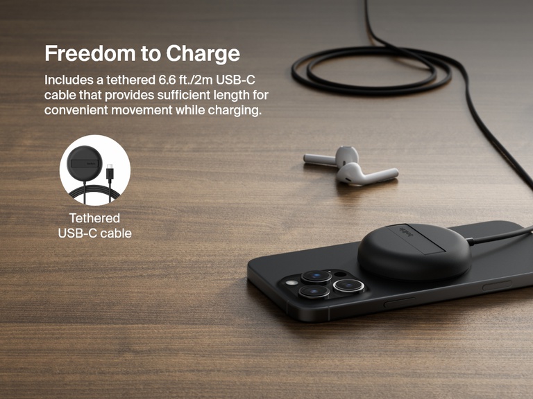 木製のテーブルの上で、Belkin BoostCharge Proマグネット式ワイヤレス充電パッド（Qi2 15W、ブラック）を使用してiPhoneを充電する様子が示されています。柔軟に配置できる長さ約2メートルの一体型USB-Cケーブルが特徴的です。