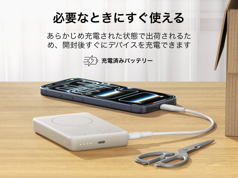 Belkin BoostCharge薄型マグネット式モバイルバッテリー10Kは、箱から出してすぐに使える状態で、USB-Cケーブルを介してスマートフォンを充電し、ポータブルバッテリーが机の上に置かれています。