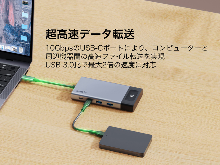 机の上に置かれたノートパソコンと外付けドライブに接続されたBelkinのUSB-Cハブ。デバイス間の10Gbpsの高速データ転送が強調されています。