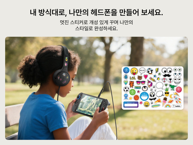 어린이가 야외에서 Nintendo Switch 2로 게임을 하면서 다채로운 스티커로 Belkin 게이밍 미니 유선 어린이용 헤드폰을 마음대로 꾸미는 모습. 자유로운 맞춤형 꾸밈과 즐거운 자기 표현을 보여줍니다.