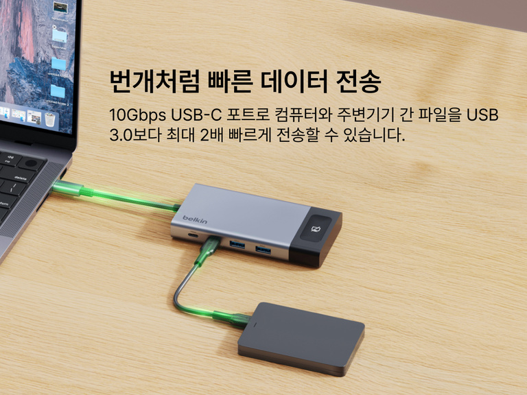 책상 위에 놓인 노트북과 외장 드라이브에 Belkin USB-C 허브를 연결한 모습으로, 장치 간 10Gbps 고속 데이터 전송을 강조합니다.