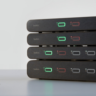 Stack of four Belkin KVM switches with illuminated port indicator lights, showcasing a multi-computer switching solution on a clean desktop.
