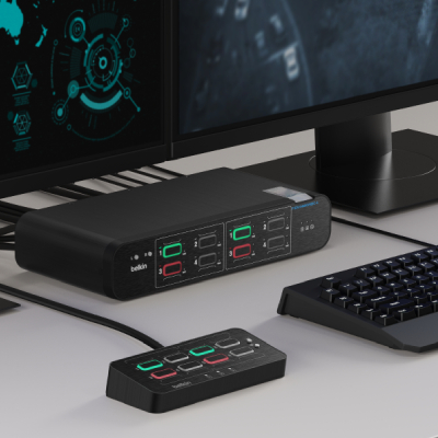 Black Belkin KVM switch and control panel on a desk setup, connected to dual monitors and a keyboard, with illuminated red and green port indicators.