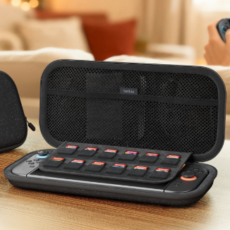 Open black Belkin Nintendo Switch carrying case on a wooden table, displaying the console with attached controllers, a built-in game cartridge organizer, and a mesh interior pocket in a living room setting.