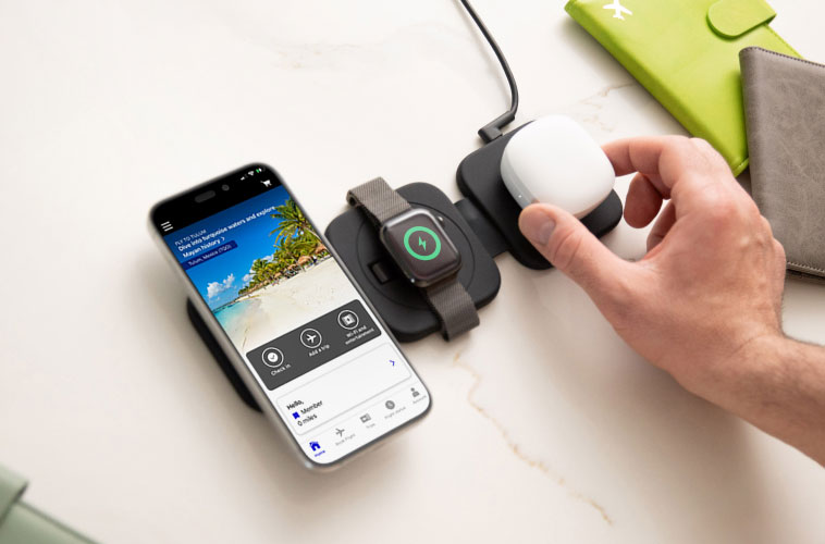 Een reiziger gebruikt een 3-in-1 MagSafe-lader om een iPhone, AirPods en een Apple Watch op te laden op een nachtkastje