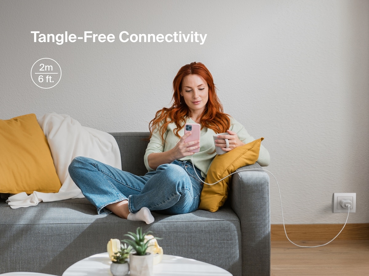Woman sits comfortably on a couch using her iPhone connected to a Belkin BoostCharge USB-A Cable with Lightning Connector, featuring a 6-foot length for tangle-free, extended reach charging.