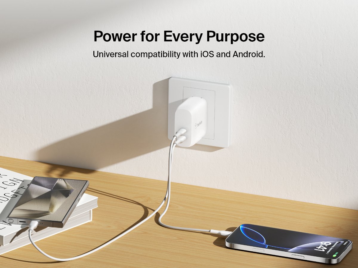 A white Belkin BoostCharge Dual USB-C PD Wall Charger 40W powers both an Android tablet and an iPhone from a wall outlet, highlighting universal compatibility with iOS and Android devices.