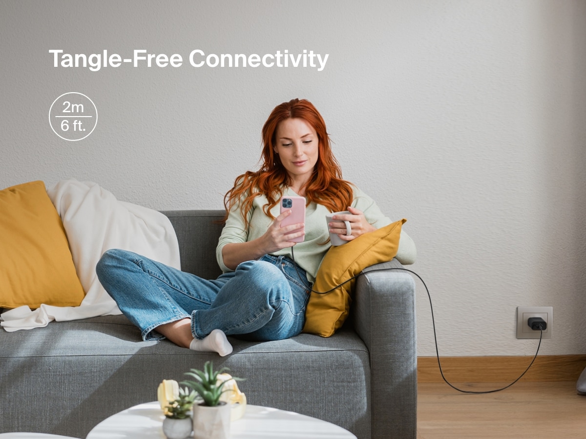 Woman sits comfortably on a couch using her iPhone connected to a Belkin BoostCharge USB-A Cable with Lightning Connector, featuring a 6-foot length for tangle-free, extended reach charging.