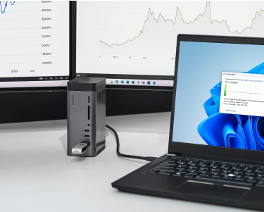  This image displays a sleek connectivity hub connected to a laptop. The hub features multiple ports, including USB slots and card readers, allowing for versatile device integration. It is situated on a desk alongside a laptop and dual monitors displaying charts and graphs, emphasizing a professional, productivity-focused setup. The background highlights a clean and organized workspace.