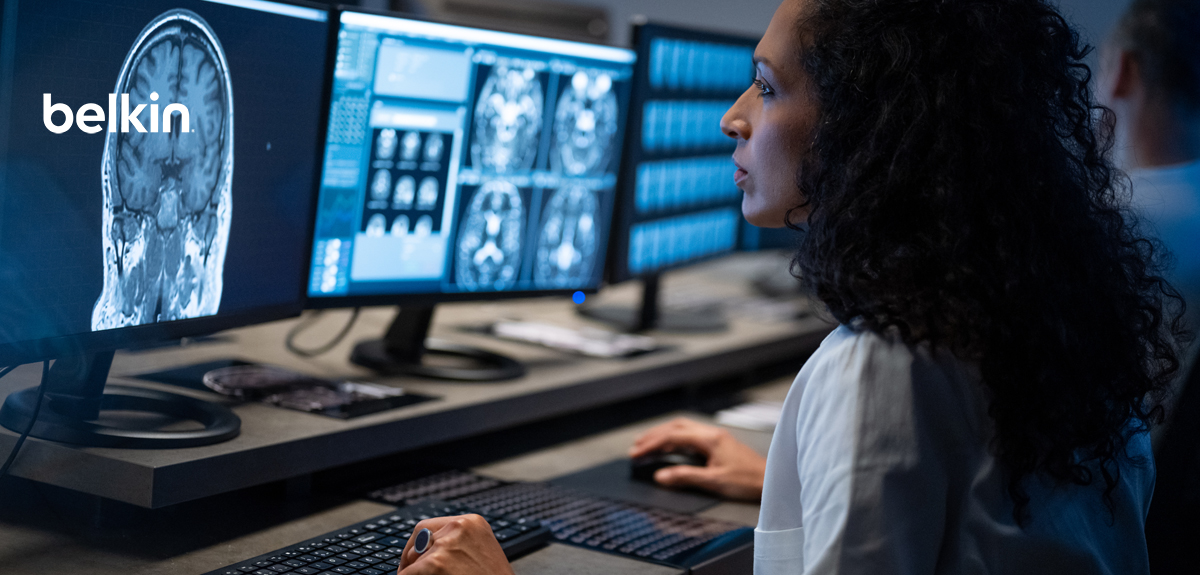 A female medical professional analyzes brain scans on multiple monitors in a dimly lit control room. The Belkin logo appears on one of the screens.