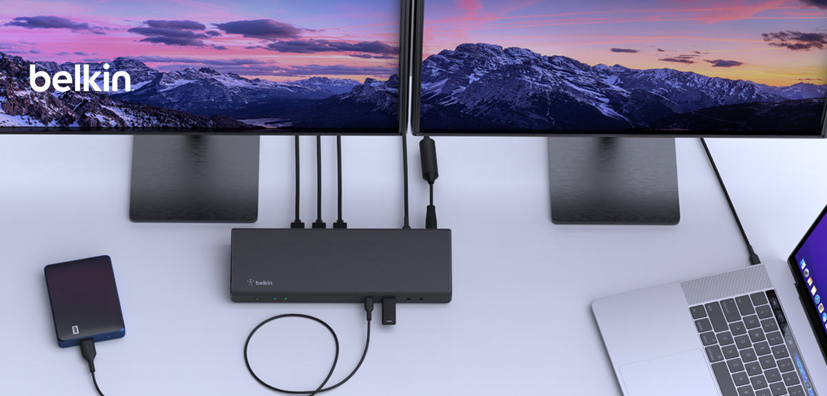 A Belkin docking station set up on a modern workspace, connecting a MacBook to dual monitors displaying a scenic mountain landscape. The docking station is also linked to an external hard drive and multiple accessories, showcasing its multi-device connectivity and expanded workstation capabilities. The sleek, organized setup emphasizes efficient cable management and productivity.