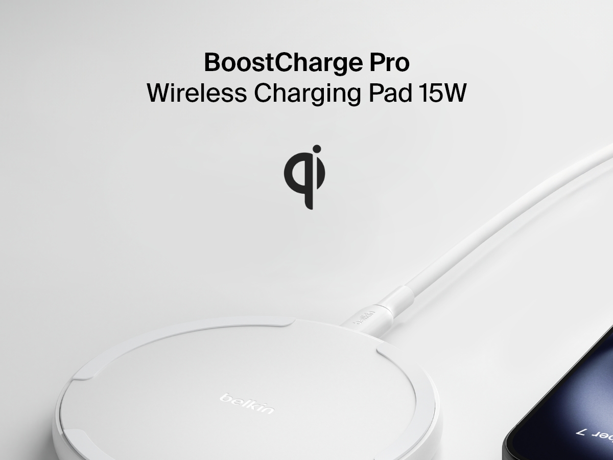 A white Belkin BoostCharge Pro Wireless Charging Pad 15W is shown in black with a connected charging cable, partially visible smartphone, and a Qi logo above the product name on a light background.