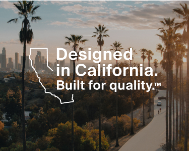 This image depicts a scenic view of a city, likely Los Angeles, California, featuring a stadium surrounded by trees in the foreground and a skyline of tall buildings in the background. The image includes palm trees and a sunset ambiance. Overlaid text reads: "Designed in California. Built for quality.&trade;" with an outline of the state of California next to the text.