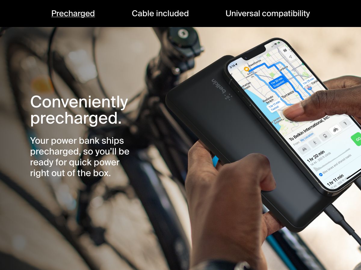 A person charges their smartphone using a black Belkin BoostCharge Power Bank 20K while navigating on a bike, highlighting its convenient precharged feature for immediate use.