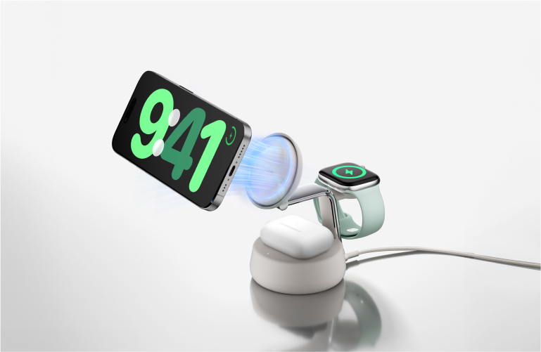 Belkin 3-in-1 wireless charging stand in white, charging an iPhone, Apple Watch, and AirPods simultaneously, with magnetic alignment shown for the phone.