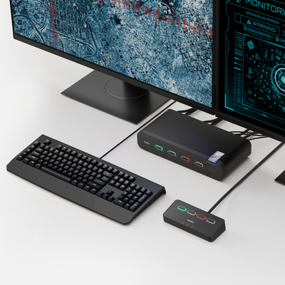 A clean desktop setup with dual monitors, a keyboard, and a compact KVM switch hub connected by cables. The KVM devices feature color-coded buttons for switching between systems, shown neatly arranged on a white desk.