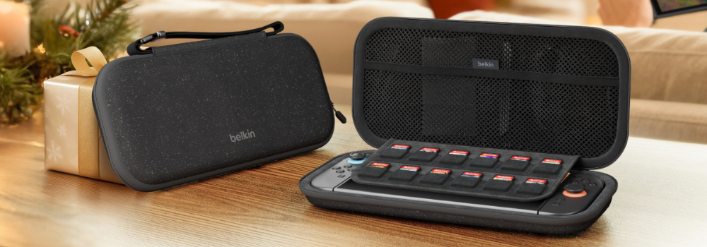 Black Belkin Nintendo Switch carrying case shown closed and open on a wooden table, with the open case holding a console, game cartridge organizer, and mesh storage pocket in a cozy home setting.