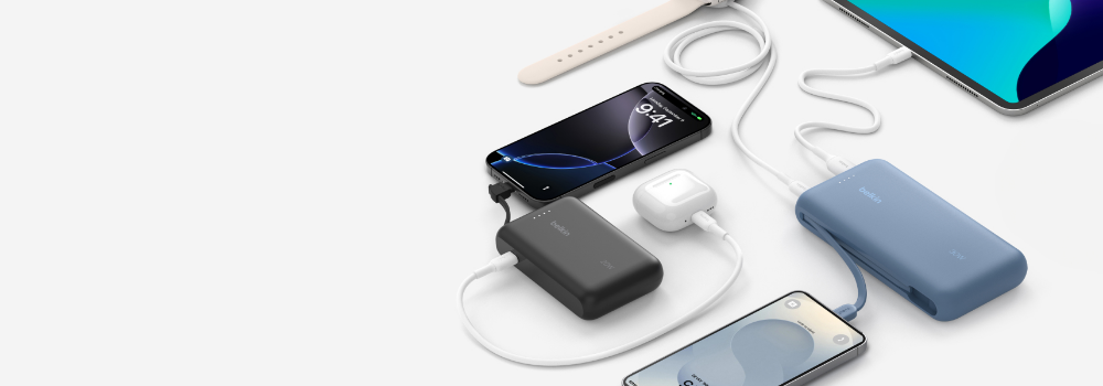 A collection of Belkin power banks in black and blue colors charging multiple devices, including smartphones, a smartwatch, wireless earbuds, and a tablet. Various charging cables are connected, showcasing the versatility of the power banks. The background is light gray, emphasizing the sleek design of the accessories.