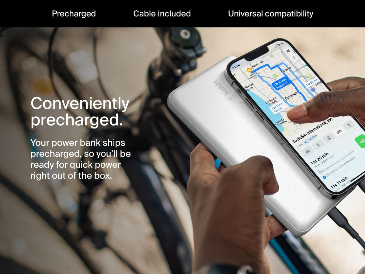 A person charges their smartphone using a white Belkin BoostCharge Power Bank 20K while navigating on a bike, highlighting its convenient precharged feature for immediate use.
