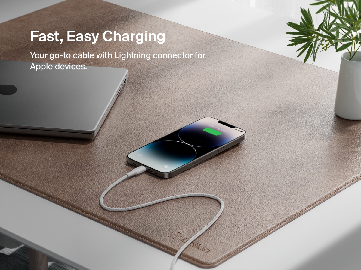 A Belkin BoostCharge Braided USB-A Cable with Lightning Connector charges an iPhone on a desk, showcasing fast, reliable charging for Apple devices.