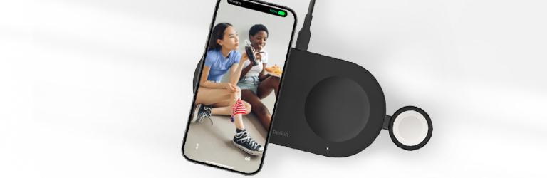 A black Belkin 3-in-1 wireless charging pad powers an iPhone, Apple Watch, and AirPods with a Memorial Day-themed image displayed on the iPhone screen.