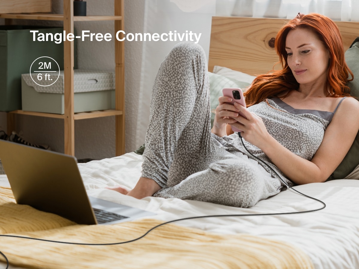 女性がベッドでくつろぎながら、iPhoneをLightningコネクタ付きのBelkin BoostCharge USB-Cケーブルに接続しています。絡まりにくい6フィートの長さで、広い範囲をカバーできるため、フレキシブルな充電に最適です。