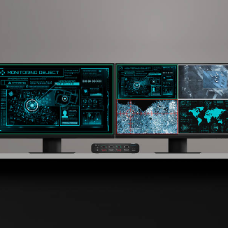 Dual-monitor setup displaying surveillance and monitoring interfaces, including maps, satellite imagery, and data dashboards. A Belkin multiclave KVM switch is positioned between the monitors, enabling secure control and source switching across multiple network environments.