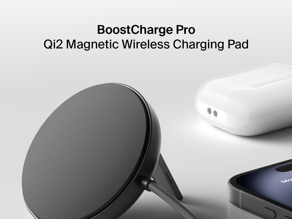 A black Belkin BoostCharge Magnetic Wireless Charging Pad with Qi2 15W is shown upright on a white surface next to an iPhone and a pair of white AirPods in their charging case.