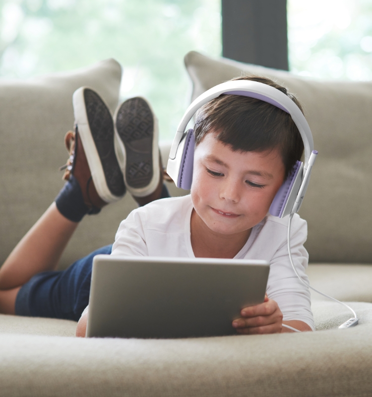 A kid wearing the headphone while he is playing with a tablet.
