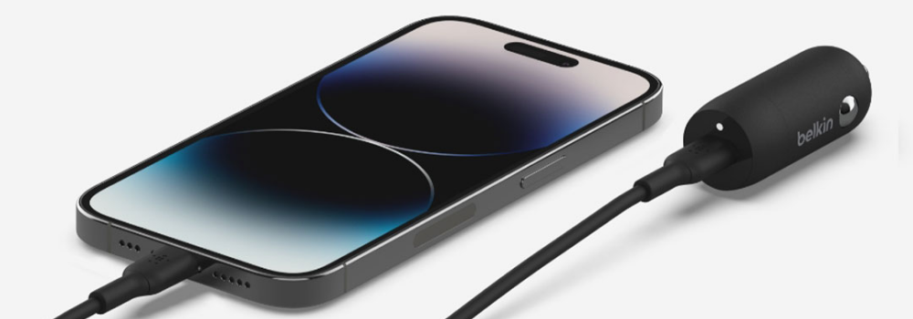 A smartphone connected to a Belkin device via USB-C cables; the phone appears to be a modern iPhone with a sleek, flat-edge design and a dynamic island at the top of the screen.