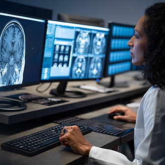 A female medical professional analyzes brain scans on multiple monitors in a dimly lit control room. The Belkin logo appears on one of the screens.