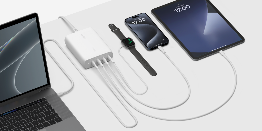 A Belkin 200W 4-Port USB-C GaN Charger on a white desk charging a laptop, a smartwatch, an iPhone and an iPad by cable