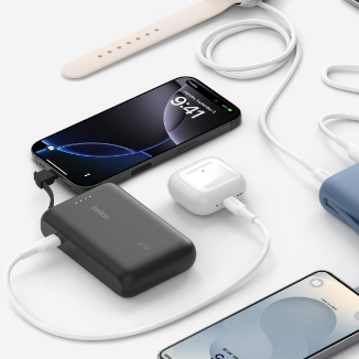 A close-up of Belkin power banks in black and blue charging multiple devices, including a smartphone, wireless earbuds, and a smartwatch. Various charging cables are connected, highlighting the versatility and convenience of the power banks for travel.